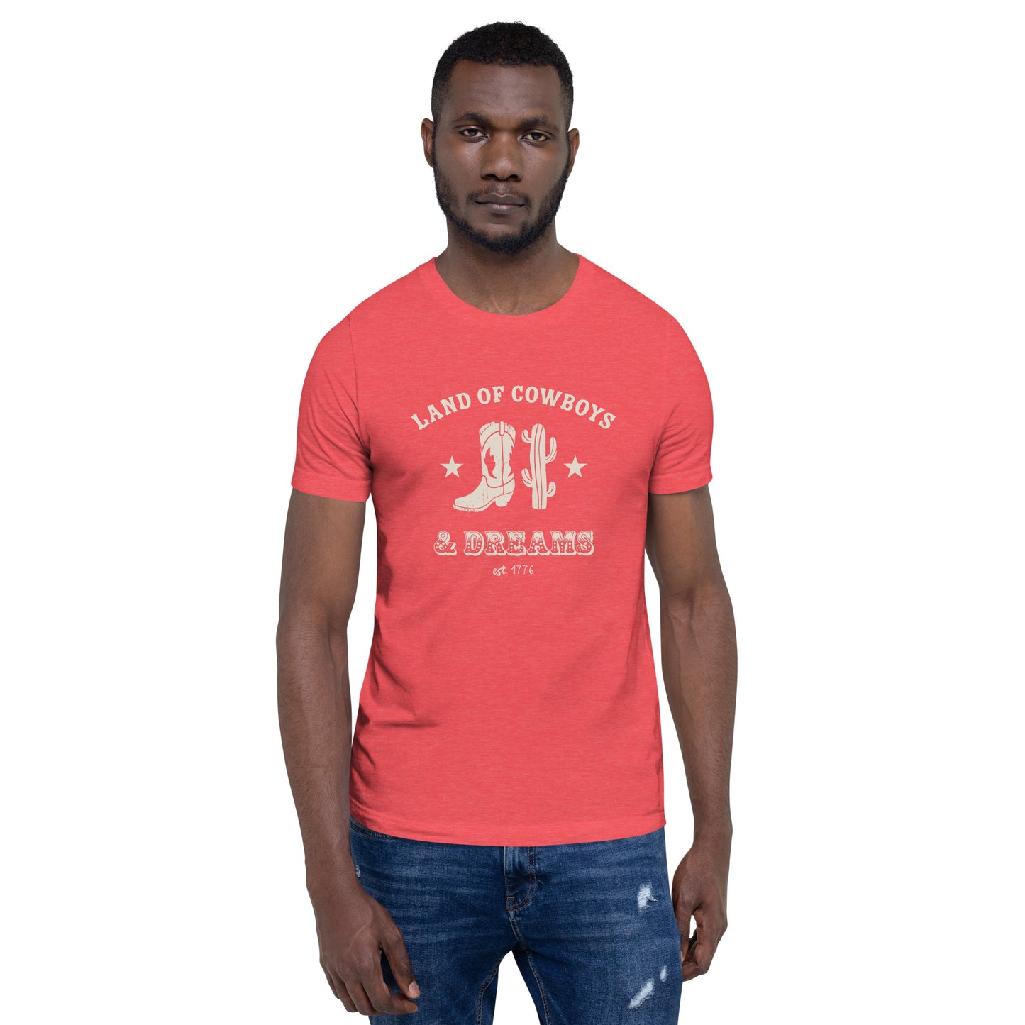 Man wearing a blue t-shirt with a white graphic featuring a cowboy boot, cactus, and text that says “Land of the Cowboys and Dreams est. 1776.”