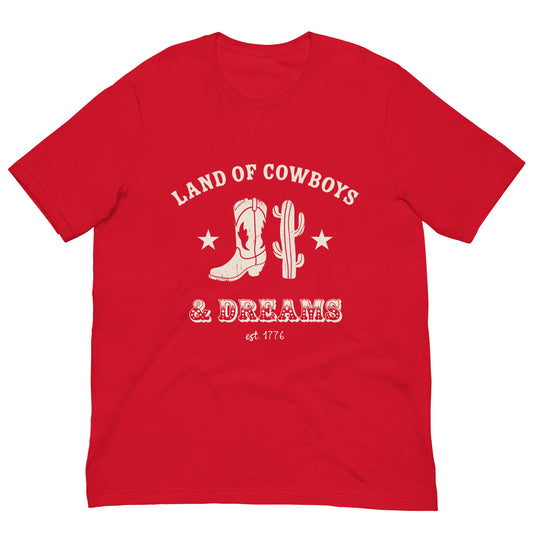 Red t-shirt with a white graphic featuring a cowboy boot, cactus, and text that says “Land of the Cowboys and Dreams est. 1776.”