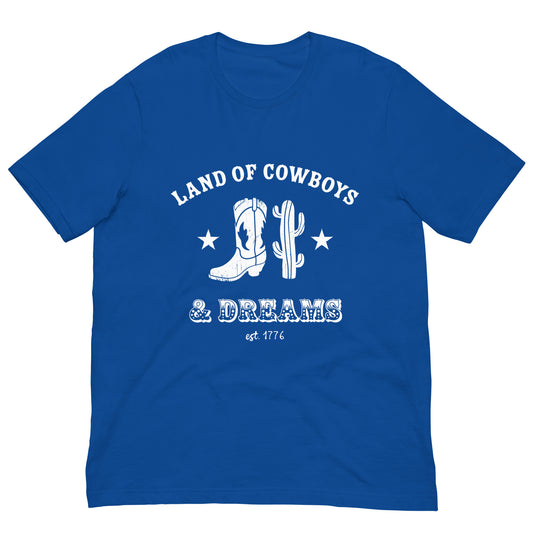 Blue t-shirt with a white graphic featuring a cowboy boot, cactus, and text that says “Land of the Cowboys and Dreams est. 1776.”