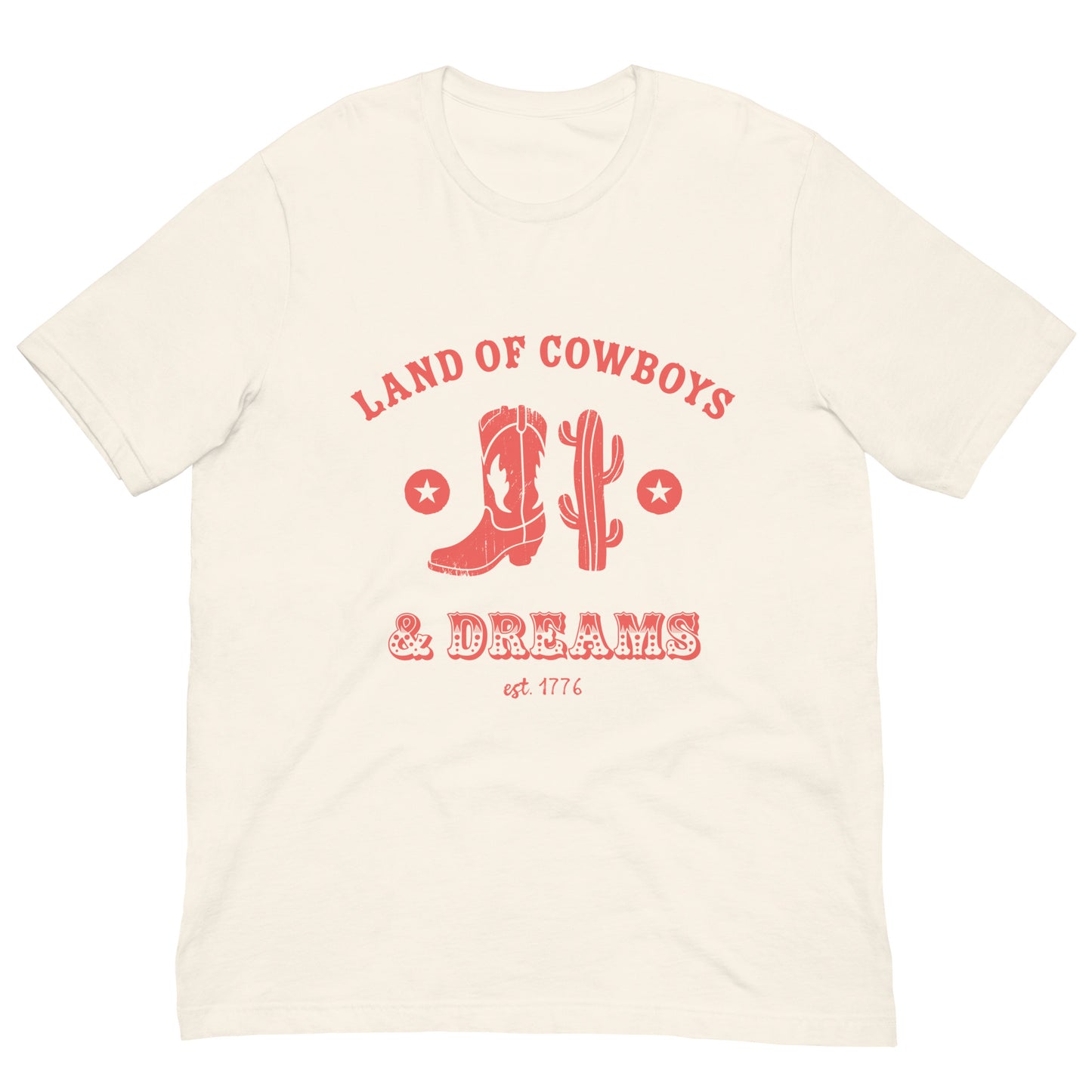 Beige t-shirt with a red graphic featuring a cowboy boot, cactus, and text that says “Land of the Cowboys and Dreams est. 1776.”