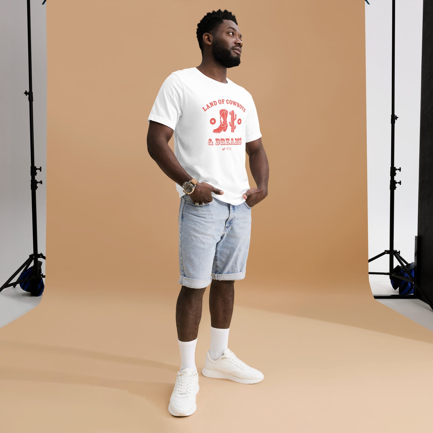 Man wearing a white t-shirt with a red graphic featuring a cowboy boot, cactus, and text that says “Land of the Cowboys and Dreams est. 1776.”